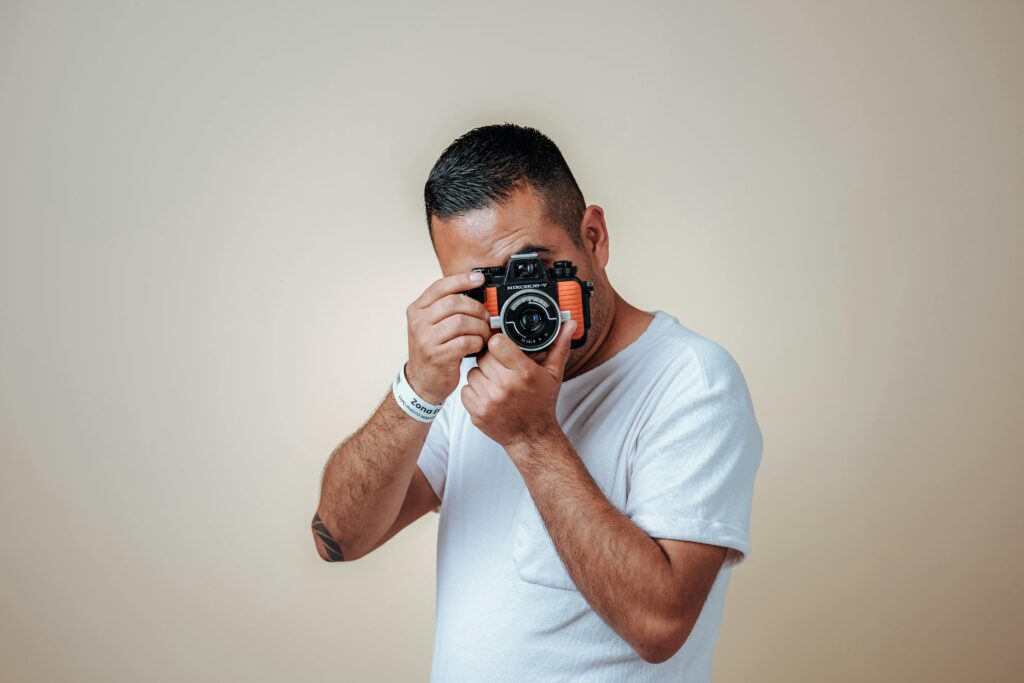 Portrait of a man holding a vintage camera against a beige backdrop, embodying a retro vibe.